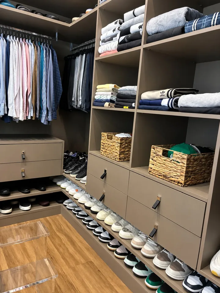 Closet masculino com camisas penduradas por cor, malhas dobradas nos nichos e tênis alinhados por categoria